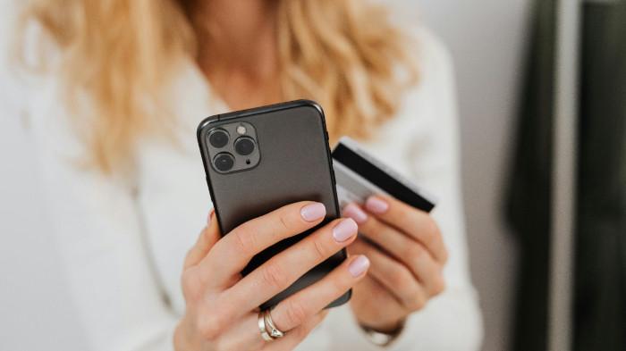 Seseorang memegang smartphone dan kartu kredit untuk melakukan transaksi belanja online